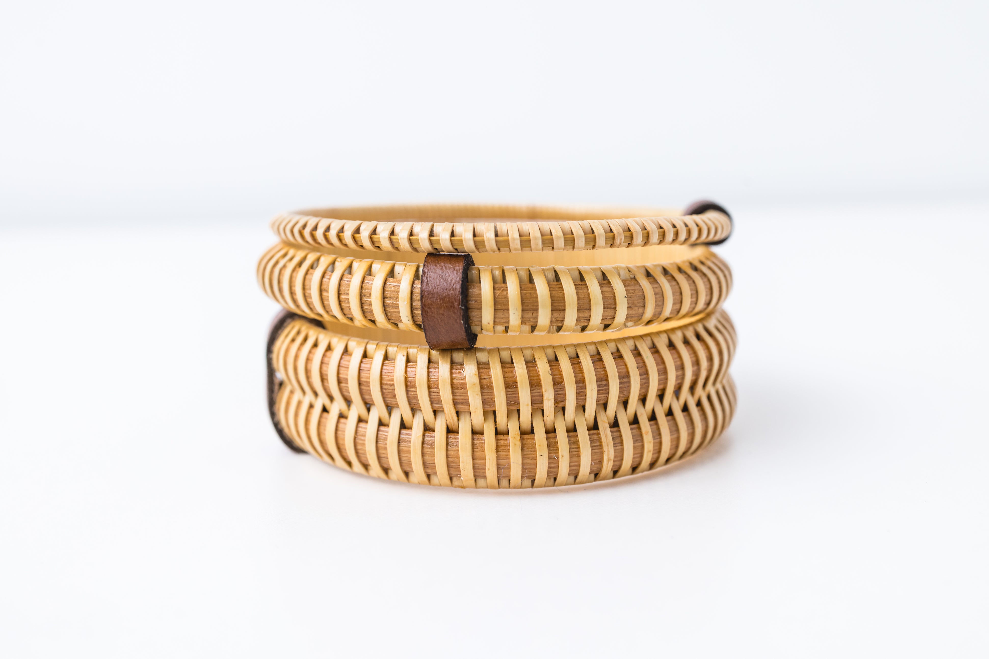 A set of three woven bangle bracelets in beige color, displayed vertically on a white background.