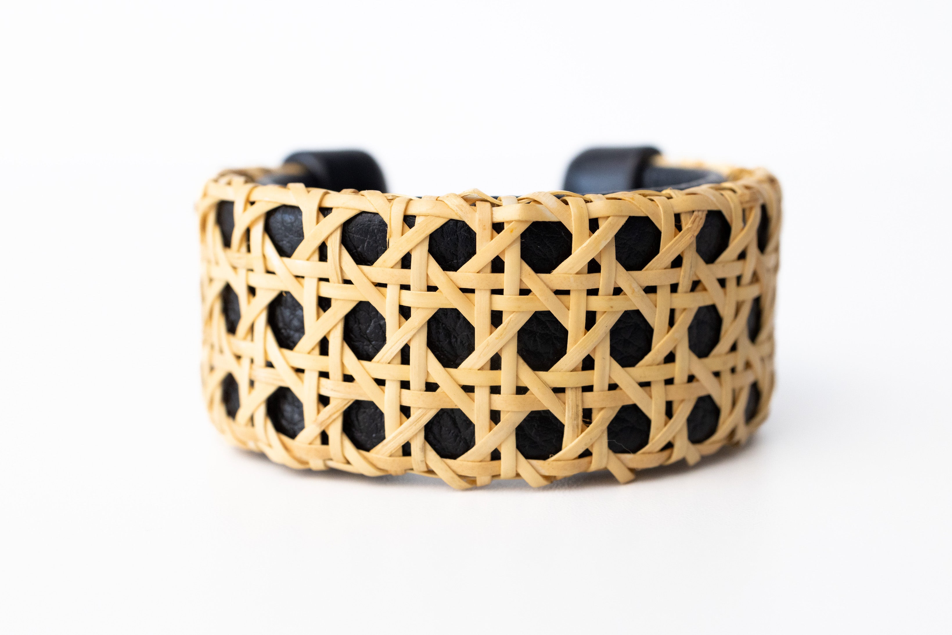A black cane cuff bracelet with Italian leather base and hand-carved wooden ends, displayed against a white background.