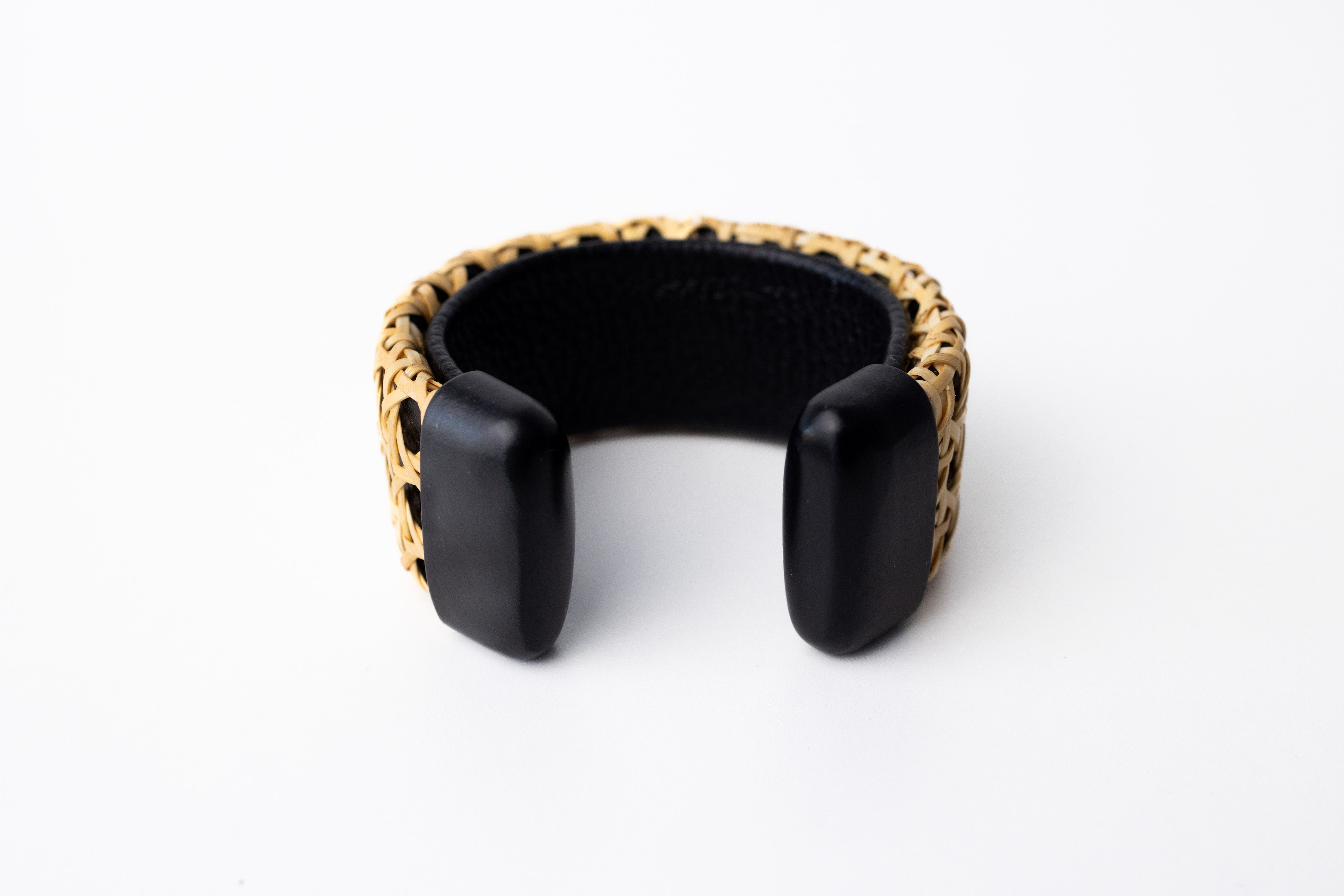 A black cane cuff bracelet with Italian leather base and hand-carved wooden ends, displayed against a white background.