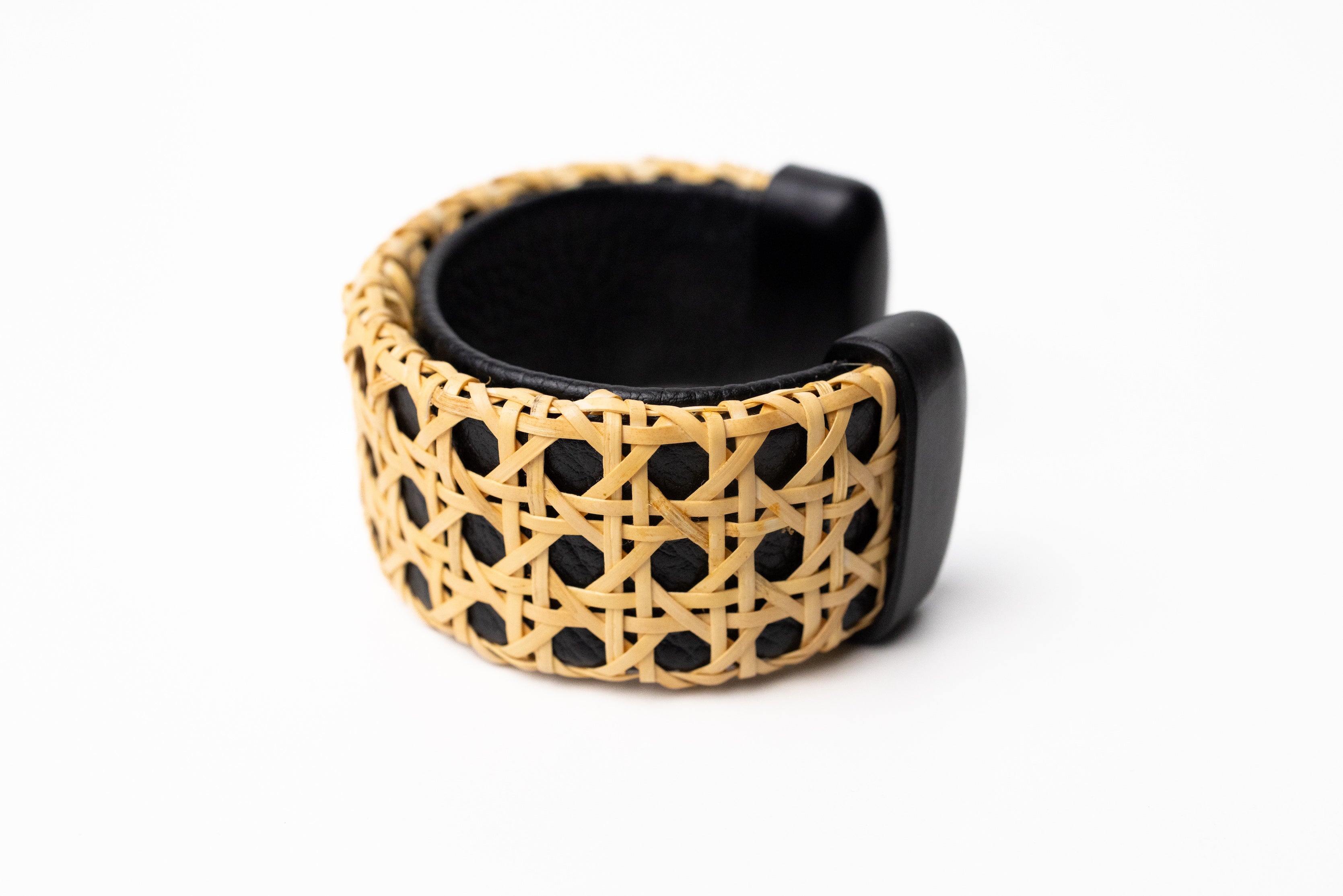A black leather cuff bracelet with a geometric pattern and wooden elements, displayed against a white background.