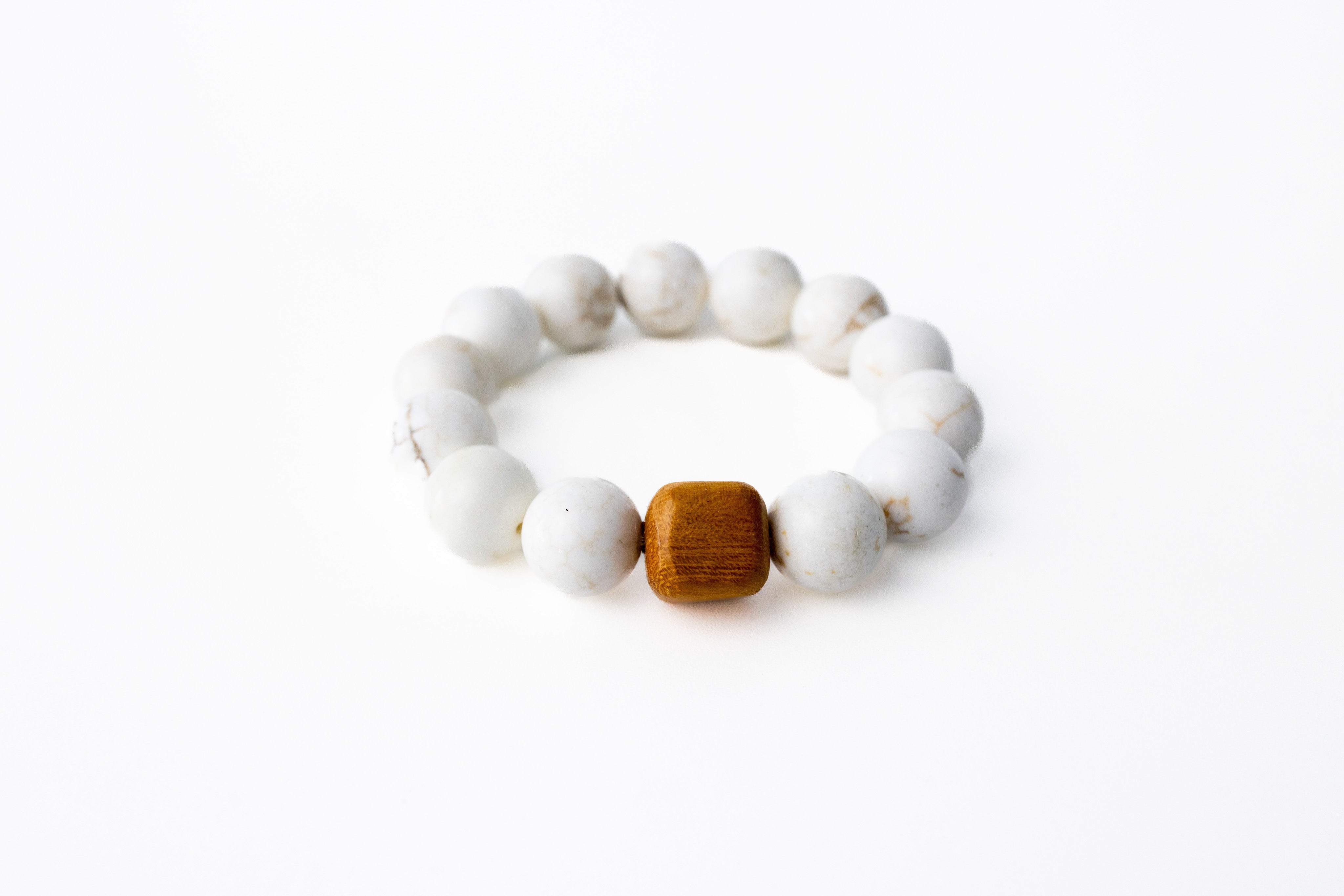 A white beaded bracelet with a brown accent piece, displayed against a white background.