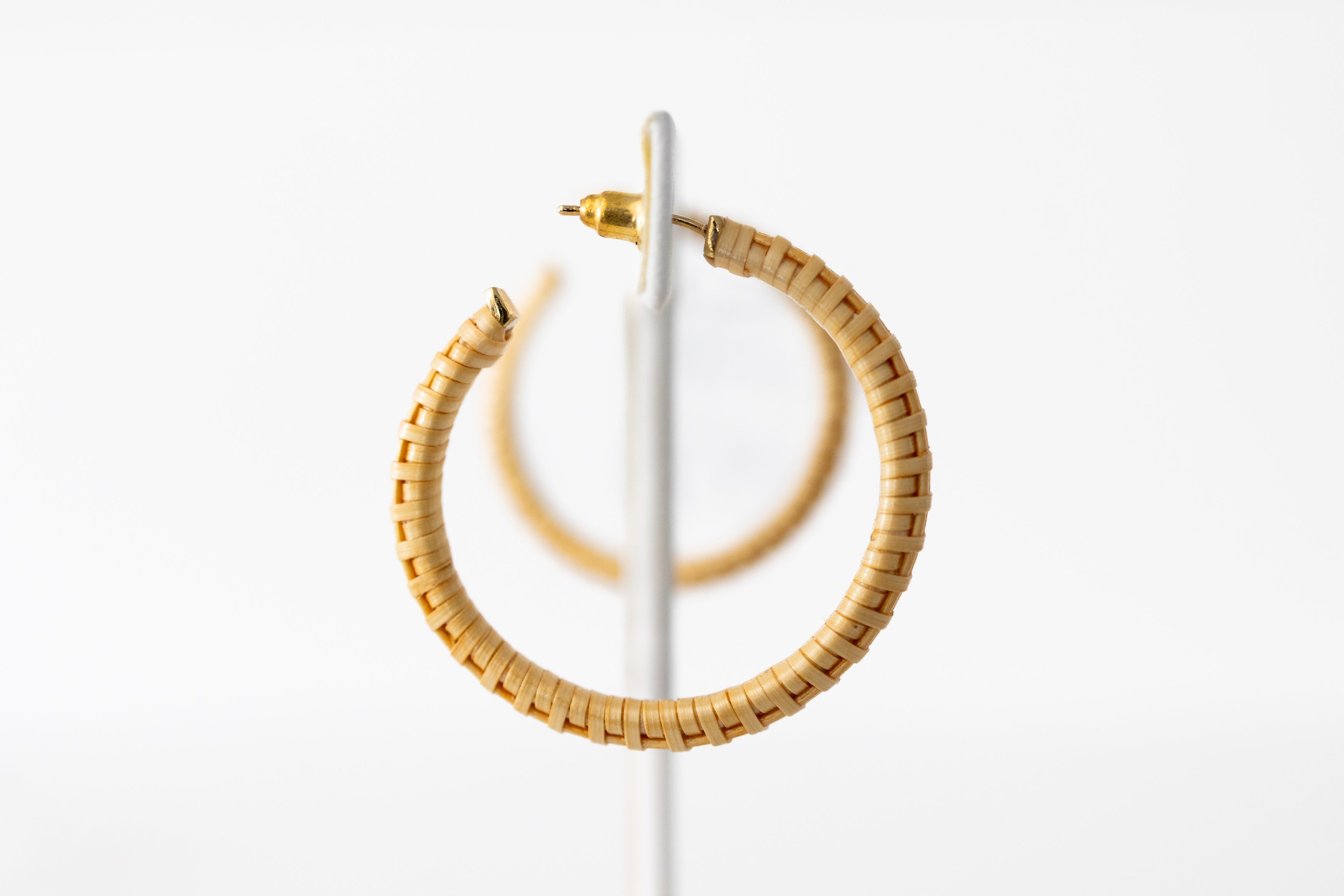 A pair of hoop earrings made of beige-colored material, displayed on a vertical stand against a white background.