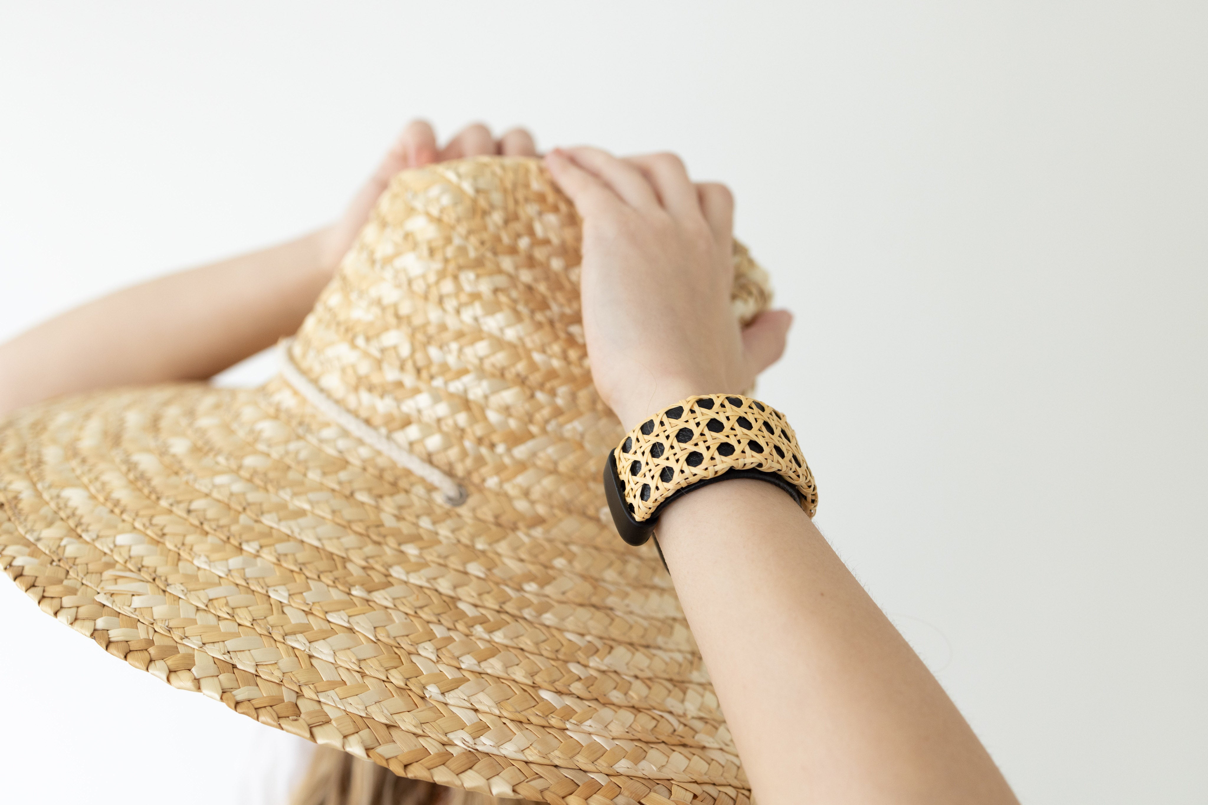 Hands holding a sunhat with a black cuff bracelet around wrist.