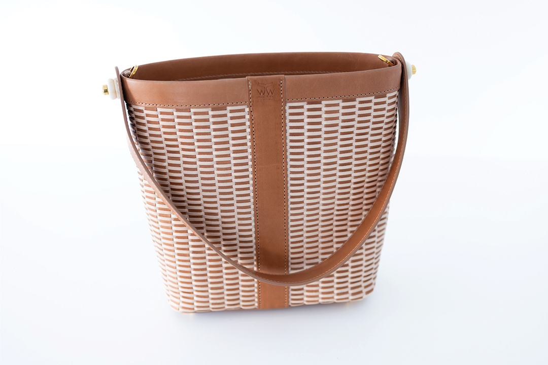 A brown leather handbag designed in the style of a Nantucket lightship basket, with a textured pattern on the sides and a flat handle.
