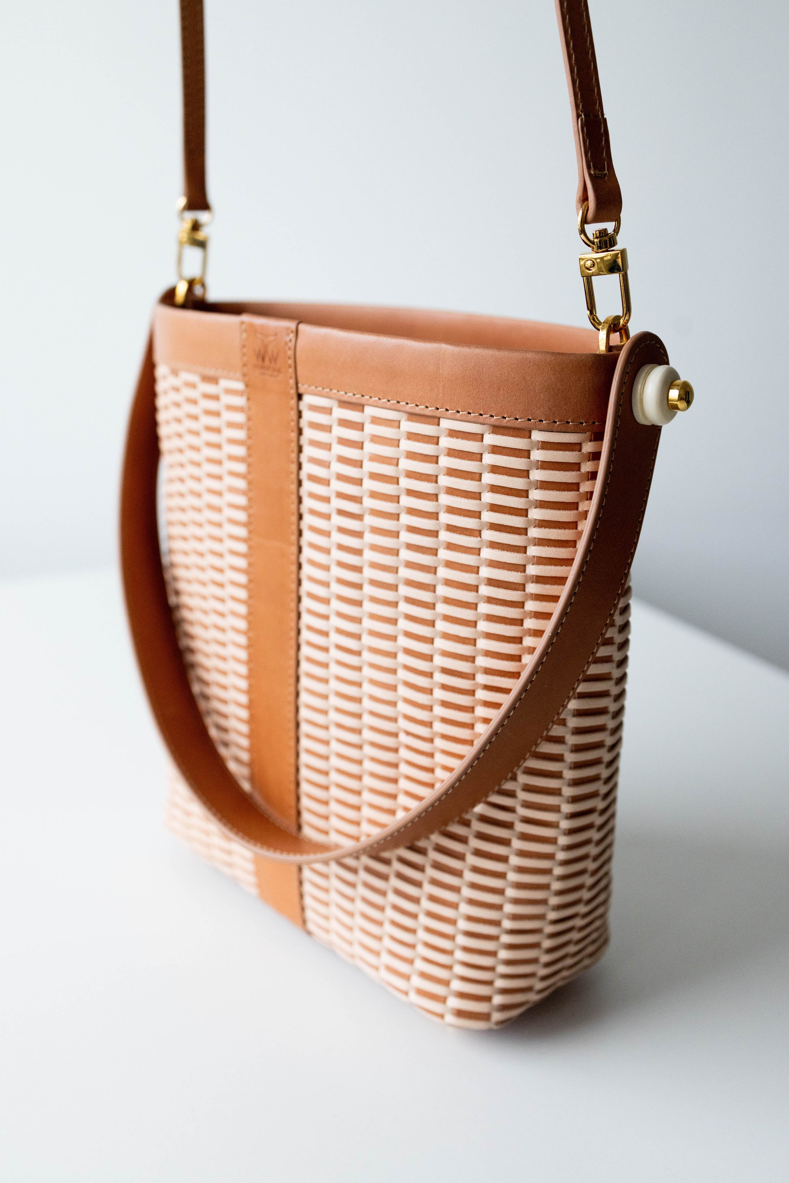 A leather handbag with a patterned design, featuring a brown strap and gold hardware, on a white background.