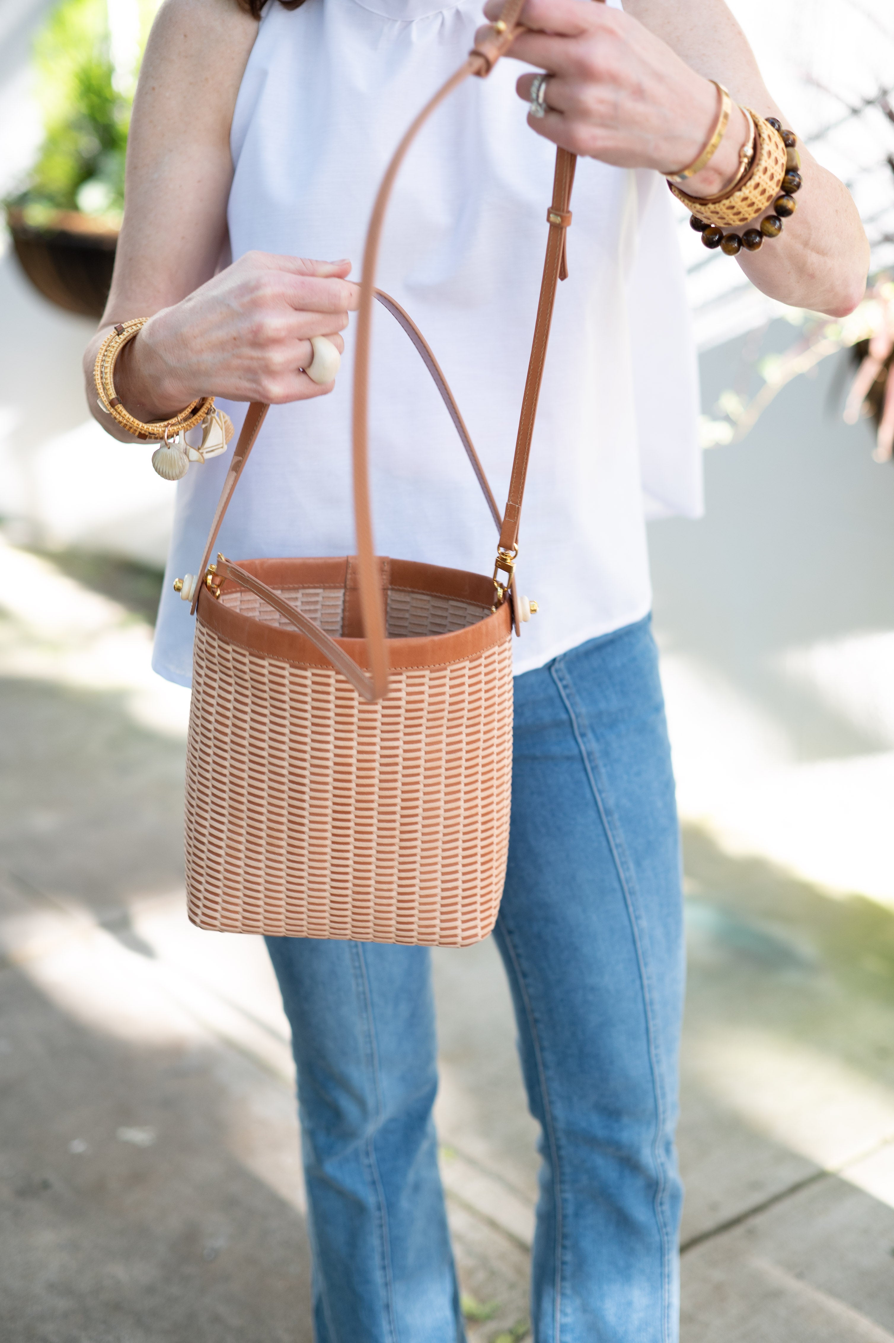 A woman in a white shirt holding the Nantucket inspired basket bag with nautical jewelry around her wrists.