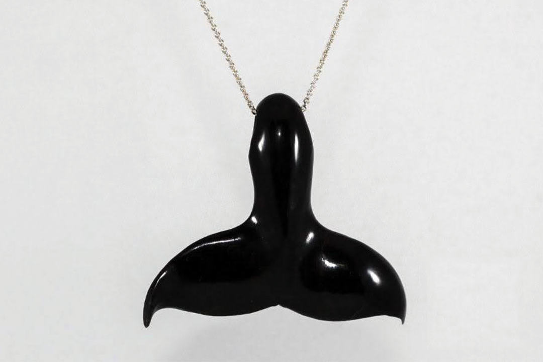 Black whale tail pendant made of ebony walrus bone, displayed on a silver chain against a white background.