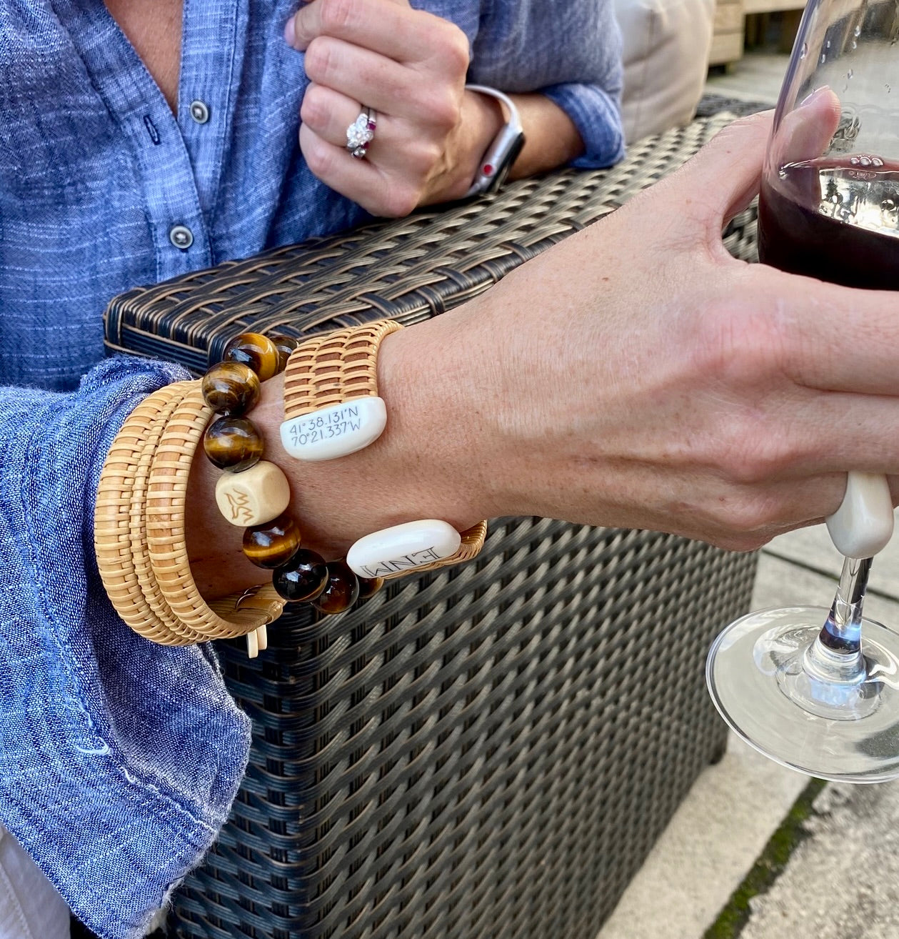 A close up of a woman holding a glass of red wine with Nantucket jewelry gifts around her wrist.