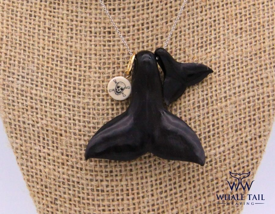 Two whale tail pendants sit against a burlap background.